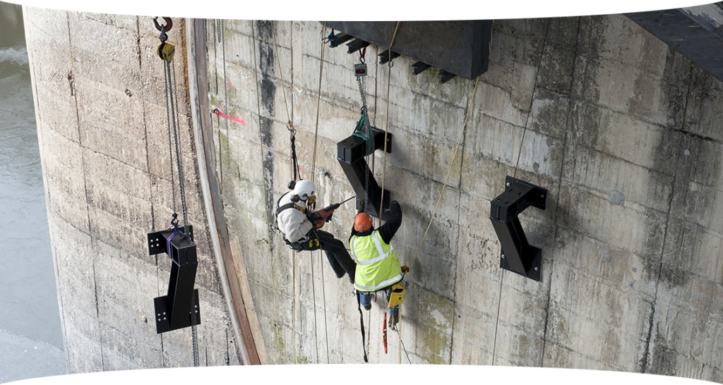 Techniciens en cordiste intervenant sur la paroi d'un barrage pour des opérations de maintenance et d'inspection